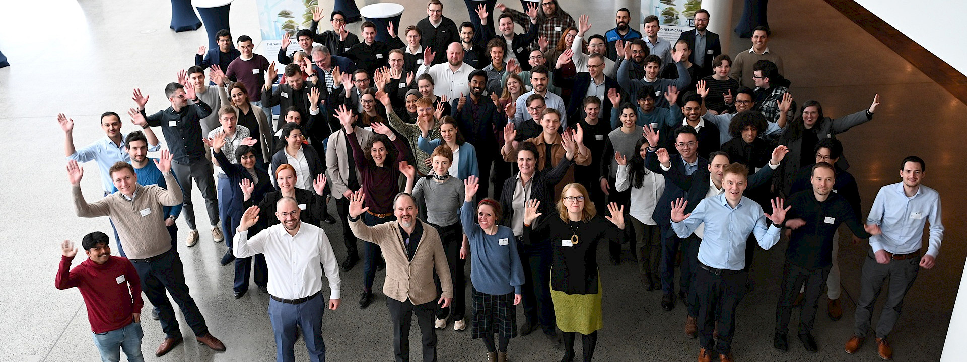 A group photo taken from above, with the participants waving at the camera.