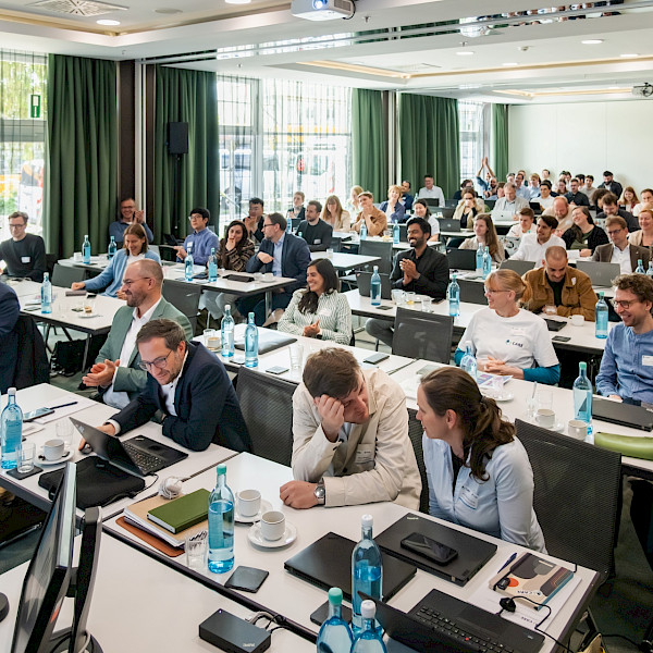 People in a room, sitting at conference tables listening to a presentation